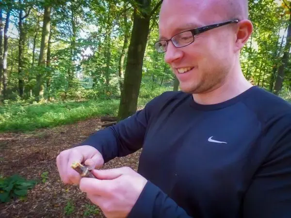 Mann bearbeitet Zunder mit einem Messer im Wald