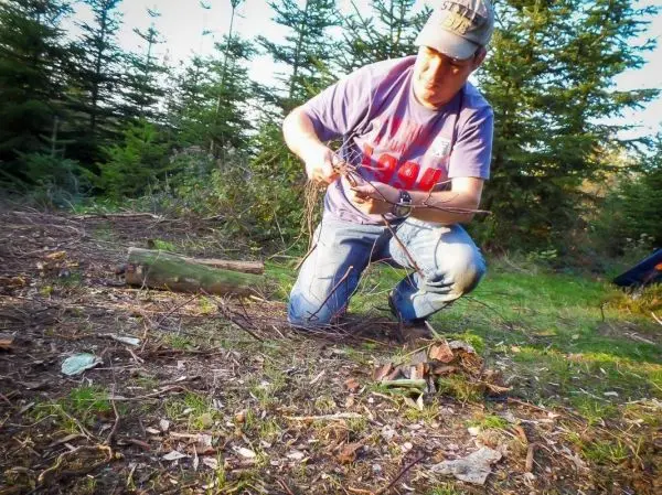 Mann bindet Äste zu einem Zundernest auf dem Boden