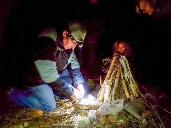 Mann entzündet Zunder vor einem kleinen Holzstapel im Dunkeln