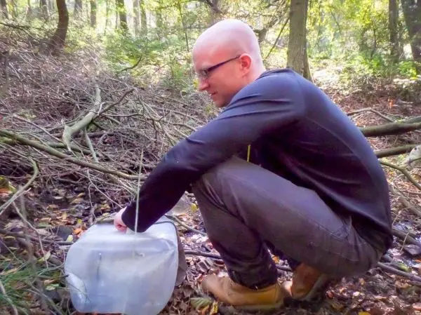 Mann kniet neben einem transparenten Behälter im Wald und greift hinein