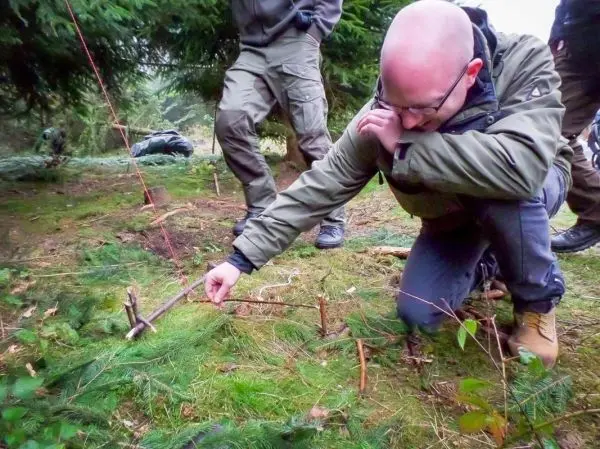 Mann kniet und platziert einen Stock für eine Schlagfalle im Wald