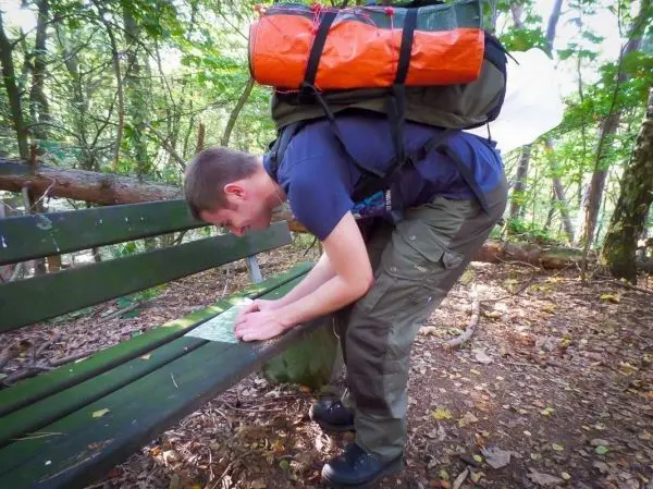 Mann mit Rucksack studiert eine Karte auf einer Bank im Wald