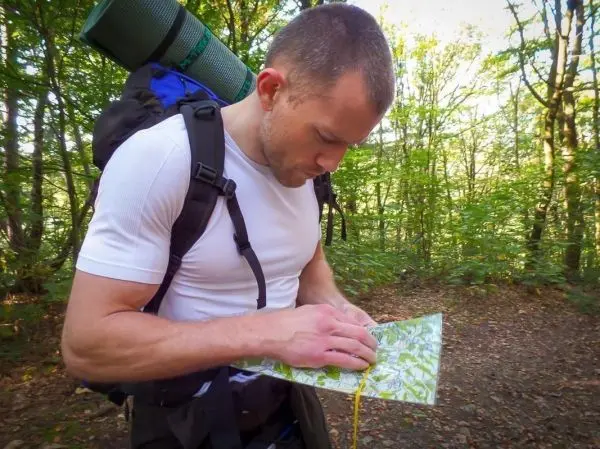 Mann studiert eine Karte im Wald, Rucksack und Isomatte auf dem Rücken