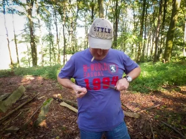 Mann zieht sein T-Shirt im Wald hoch, um etwas zu zeigen