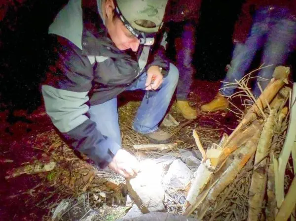 Mann zündet Zunder mit Taschenlampe neben Holzstapel im Dunkeln