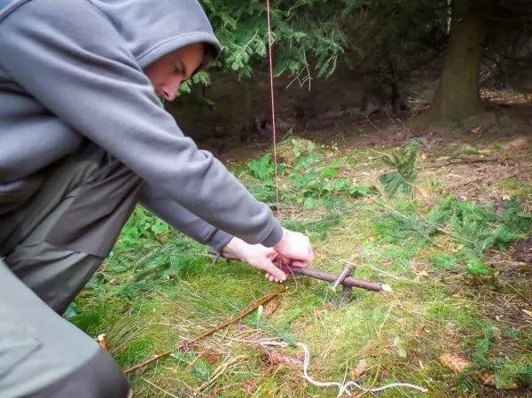 Person befestigt eine Schnur an einem Stock im Wald