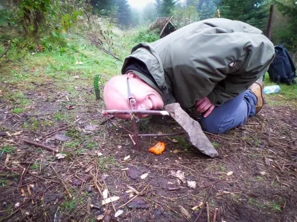 Person beugt sich über eine selbstgebaute Falle im Wald