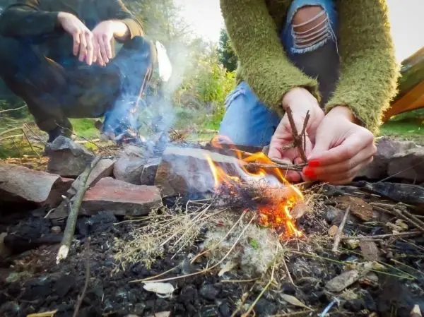 Person entzündet Feuer mit Zweigen beim Survival Training