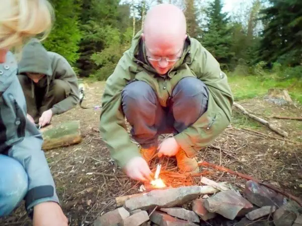 Person entzündet Feuerstelle mit Zunder im Wald beim Survival Training