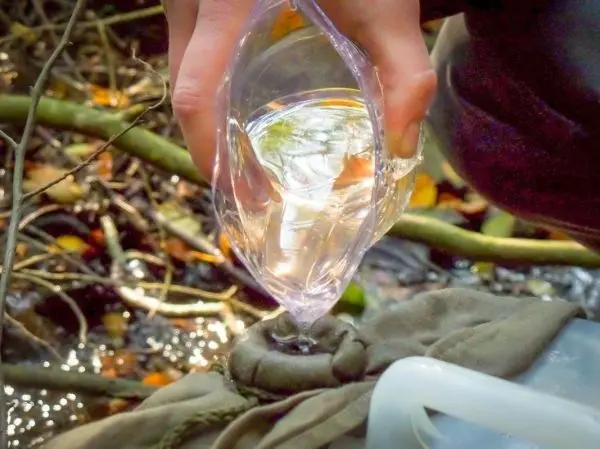 Person gießt Wasser in einen Behälter im Wald