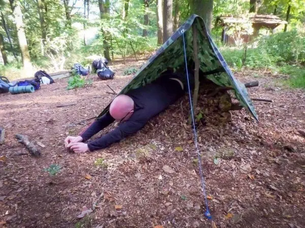 Person kriecht unter einer selbstgebauten Plane im Wald