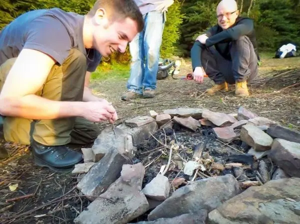 Person zündet Feuerstelle mit kleinen Ästen an beim Überlebenstraining