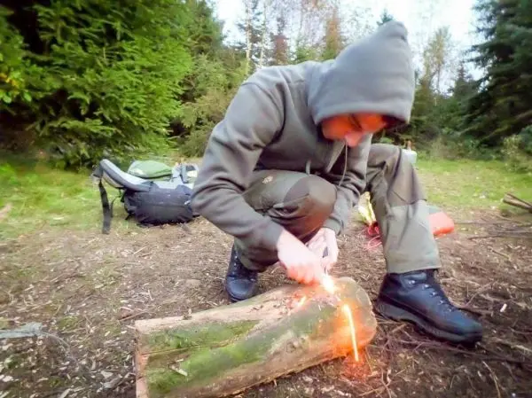Person zündet Holzstück mit Feuerzeug an beim Survival Training