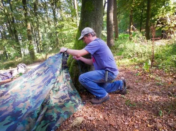 Tarp-Notunterkunft wird an einem Baum befestigt