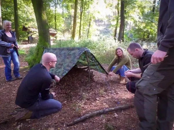 Tarp-Notunterkunft wird mit Abspannschnur zwischen Bäumen gesichert