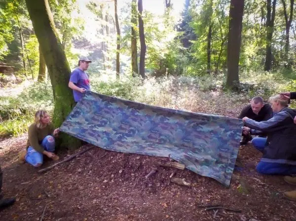 Tarp-Notunterkunft wird zwischen Baum und Untergrund gespannt