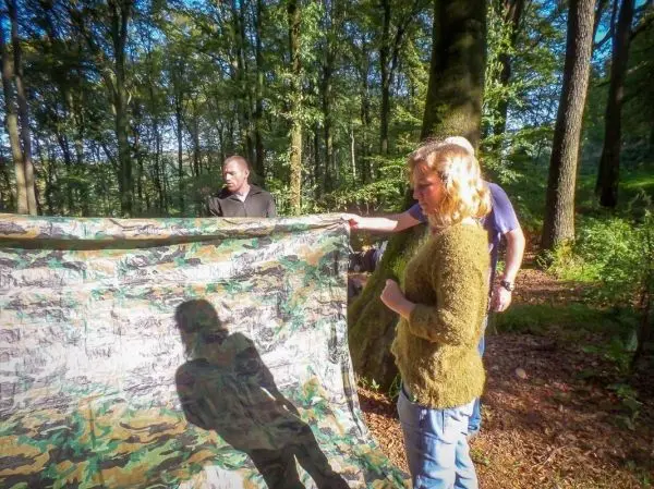 Tarp-Notunterkunft wird zwischen zwei Bäumen gespannt, während Personen helfen