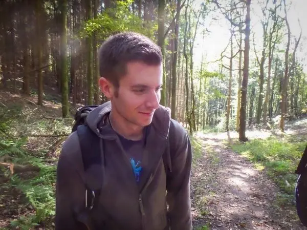 Waldweg mit Lichtstrahlen, Person trägt Rucksack und schaut nach unten