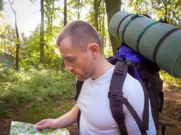 Wanderer studiert Karte im Wald, Rucksack mit Isomatte auf dem Rücken