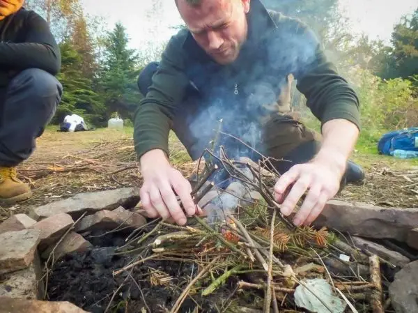 Zunder glimmt in einem Steinkreis, während Holzstücke hinzugefügt werden