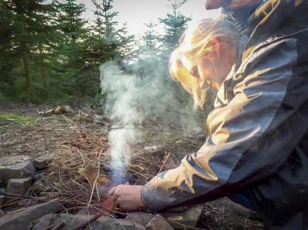 Zunder glimmt zwischen Ästen und Rauch steigt auf