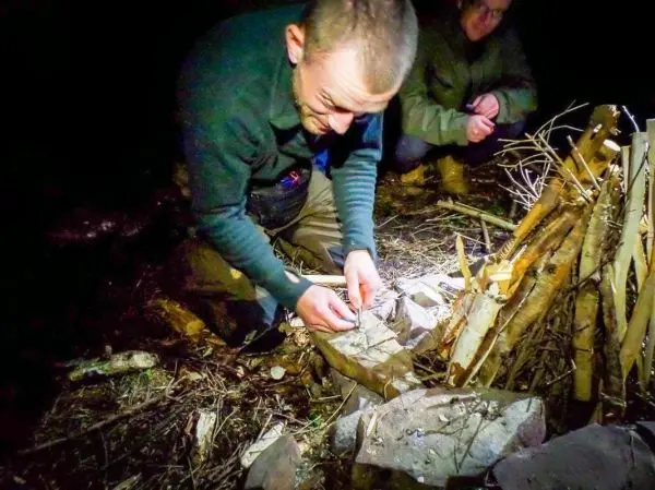 Zunder wird auf einem Stein vorbereitet, während eine Feuerstelle in der Nähe aufgebaut ist