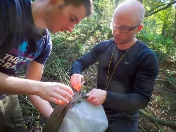 Zwei Personen befestigen eine Tarp-Notunterkunft im Wald