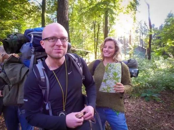 Zwei Personen stehen im Wald, eine hält eine Karte, der andere hat einen Rucksack