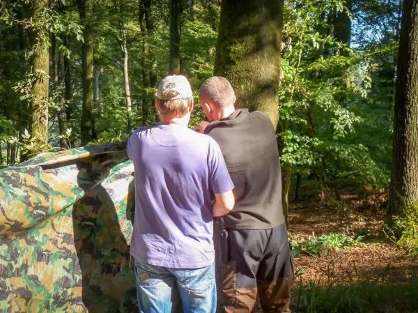 Zwei Personen stehen vor einer camouflagefarbenen Plane im Wald