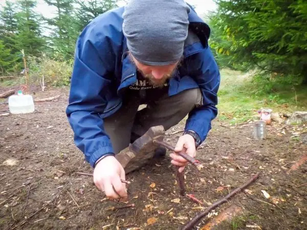 Zweige werden mit einem Stein bearbeitet, um Zunder vorzubereiten