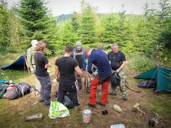 Gruppe arbeitet an einer Holzstruktur im Camp, Rucksäcke und Ausrüstung liegen verstreut