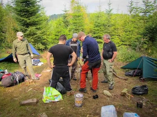 Gruppe arbeitet an einer Holzstruktur im Wald, Ausrüstung und Zelte im Hintergrund