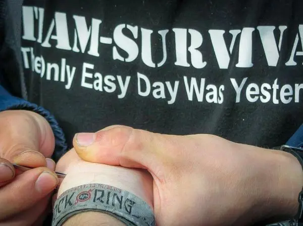 Hände halten eine Nadel über ein Handgelenk mit einem Armband