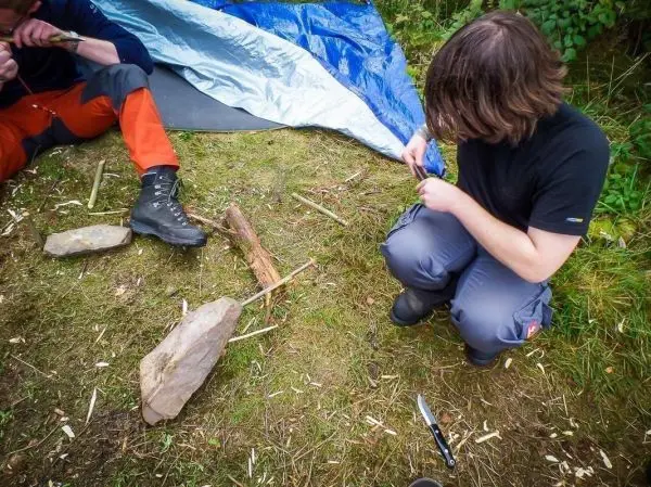 Holzstück wird mit einem Messer bearbeitet, während ein weiterer Stein daneben liegt