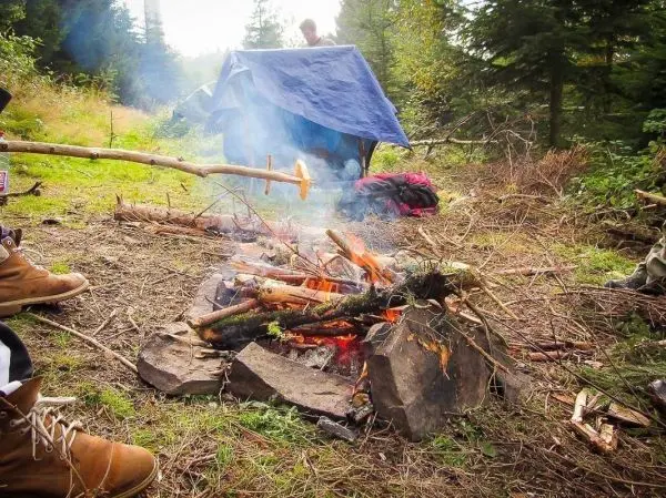 Kleine Flamme brennt zwischen Steinen, daneben liegt ein Stock mit Zunder