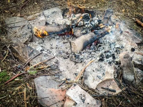 Kleine Flamme in einem Feuerkreis aus Steinen und Holzresten