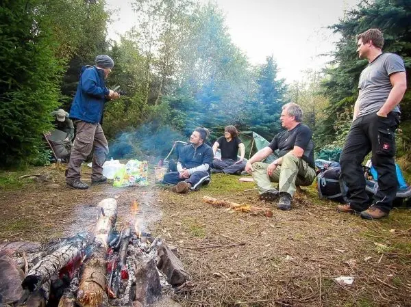 Kleines Bodenfeuer mit glühenden Holzscheiten, Gruppe sitzt im Kreis auf dem Boden