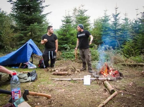 Kleines Bodenfeuer mit Rauch und zwei Personen in der Nähe der Tarp-Notunterkunft