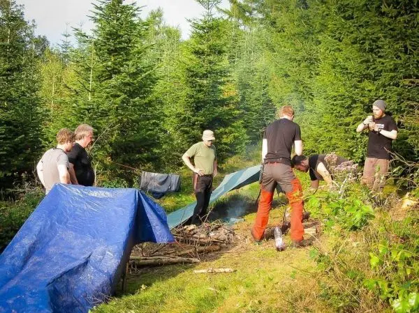Lager mit zwei Tarp-Notunterkünften und mehreren Personen um ein kleines Bodenfeuer