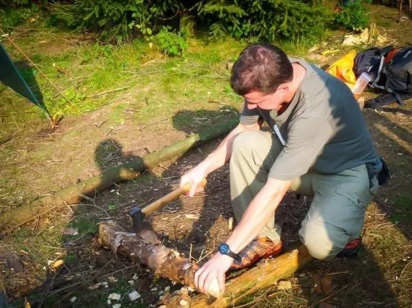 Mann bearbeitet Holzstück mit Axt auf dem Boden
