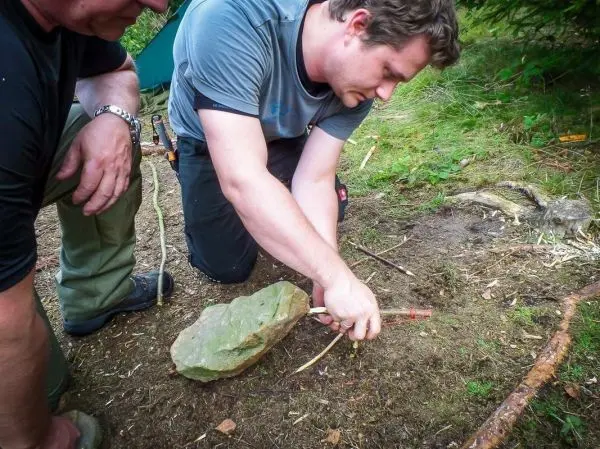 Mann bearbeitet Holzstück mit Steinwerkzeug auf dem Boden