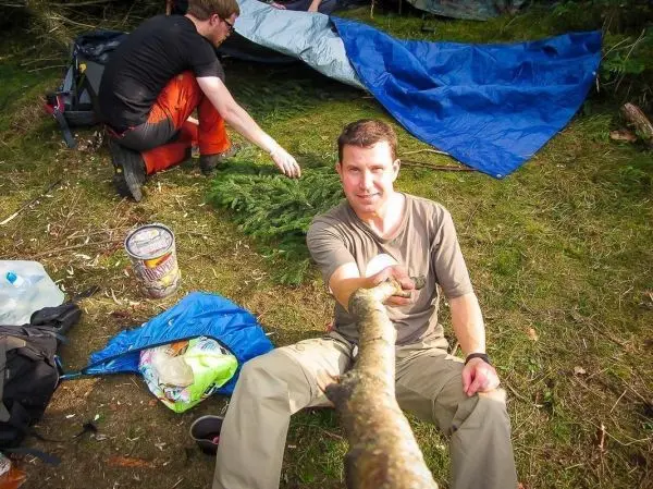 Mann hält einen Stock, während im Hintergrund eine Tarp-Notunterkunft aufgebaut wird