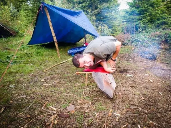 Mann lehnt sich auf eine Holzplatte vor einem Tarp und lächelt