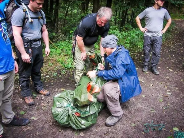 Mann packt Ausrüstung in eine grüne Tarp-Notunterkunft im Wald