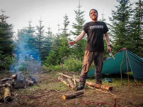 Mann steht neben einem kleinen Feuer und hält ein Messer in der Hand