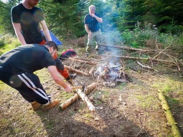 Messer hackt Holzstücke neben einem kleinen Feuer im Wald