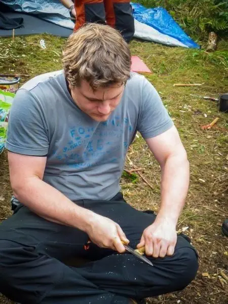 Messer schnitzt Holzstück während auf dem Boden gesessen wird