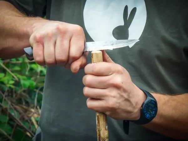 Messer schnitzt in einen Holzstock, während die andere Hand stabilisiert