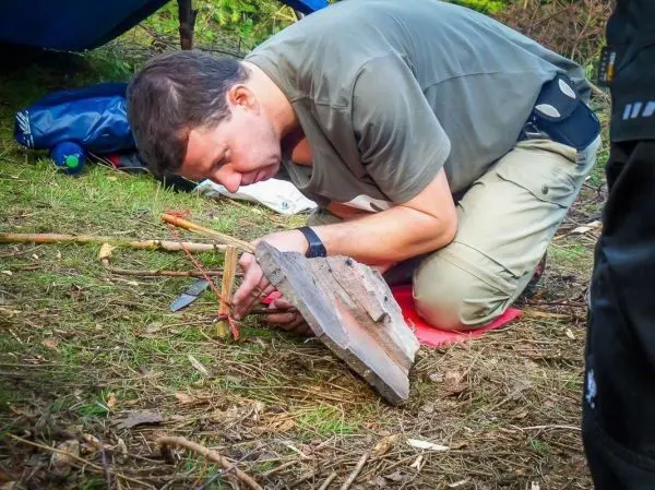Person bearbeitet Holzstücke mit einem Messer beim Überlebenstraining