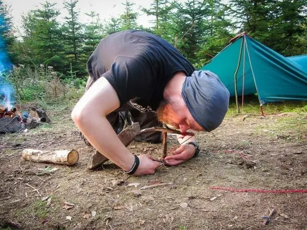 Person erzeugt Feuer mit einem Feuerbohrer im Wald beim Survival Training